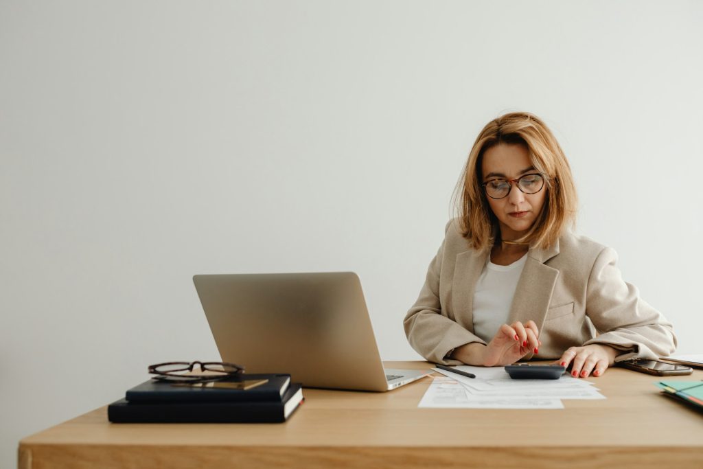 Professional woman managing financial documents at desk with laptop, glasses, and calculator, representing financial consulting and advisory services by Daybook Financial Group.