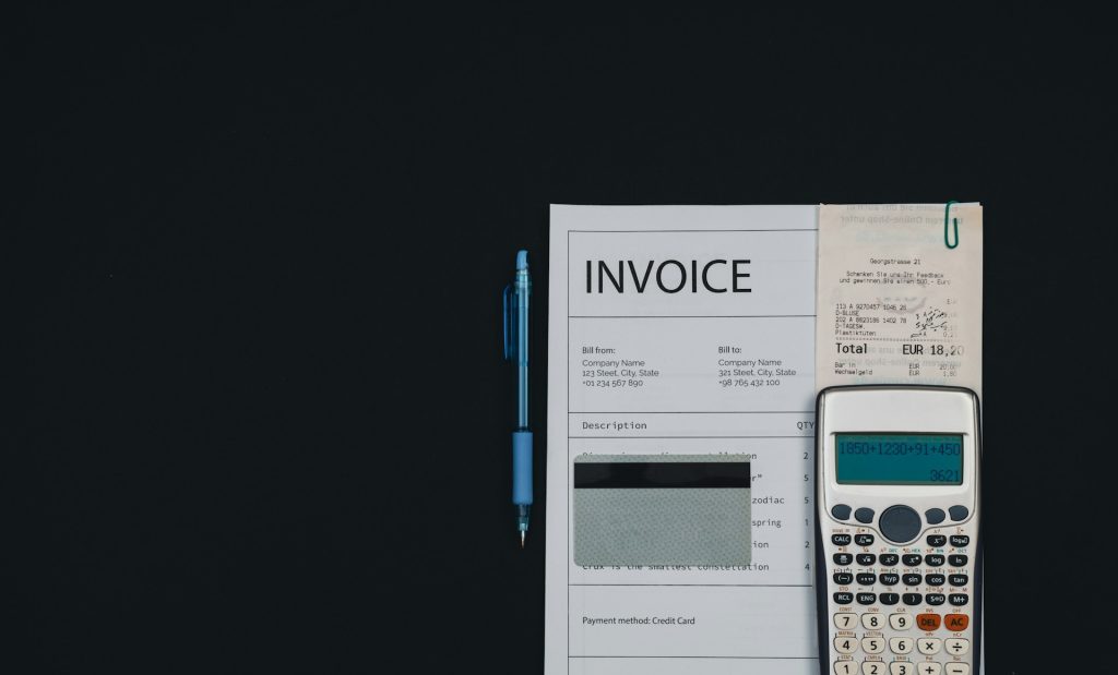 Invoice document with calculator, pen, and receipt on dark background for financial planning and accounting services.